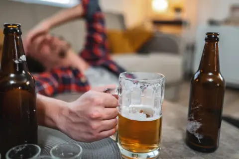 Mężczyzna leży na kanapie, trzymając kufel piwa. Wokół butelki piwa. Zastanawiasz się, ile % ma wódka?