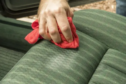 Dłoń z czerwoną ściereczką czyści zieloną tapicerkę. Domowy płyn do czyszczenia tapicerki działa cuda!