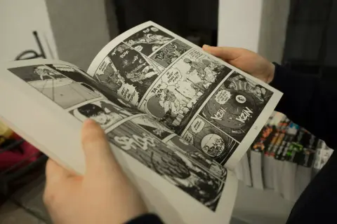 Des mains tiennent un manga ouvert, révélant des cases de bande dessinée pleines d'action. Apprendre comment lire un manga est facile avec ces images dynamiques.