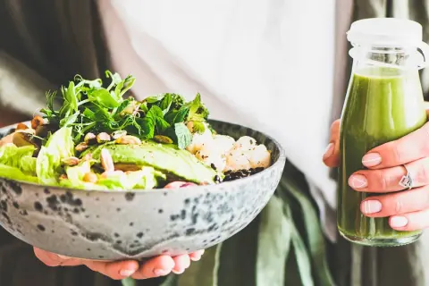 En person håller en skål med en hälsosam sallad och en grön smoothie. Perfekt bra mat gravid för näring och energi.
