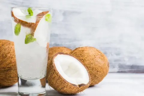 Orzeźwiający drink z wodą kokosową, lodem i miętą, obok świeżych kokosów. Idealny na upalne dni.