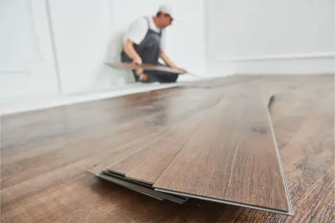 Instalador colocando tablas de vinilo SPC en un suelo de madera.