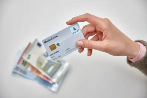 Hand hält Girocard über Euro-Scheine. So einfach ist es, mit EC-Karte im Ausland zu bezahlen und Bargeld zu sparen.