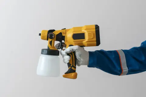 Mano guantata impugna una pistola per verniciatura a spruzzo gialla e nera, pronta per un lavoro di finitura impeccabile.