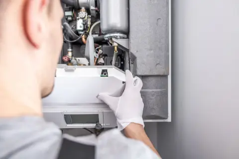 Tecnico con guanti bianchi effettua la revisione della caldaia, controllando i componenti interni.