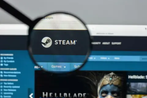 Lupa powiększa logo Steam i fragment strony internetowej platformy z grami.
