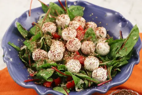 En blå skål med en sallad av gröna blad, körsbärstomater och små, kryddade labneh bollar.