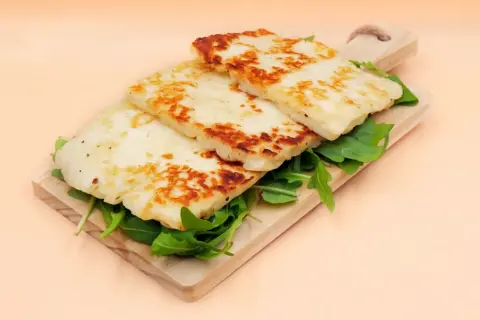 Usmażony ser halloumi na desce z rukolą.