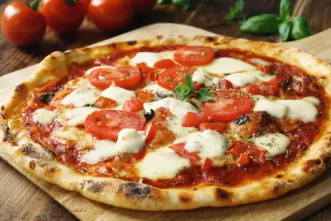 Pyszna pizza Margherita z pomidorami i rozpływającym się **serem di bufala**, ozdobiona świeżą bazylią.