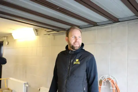 Man i väst med texten "Garageportexperten" ler. Ovanför syns en **täta garageport** i taket.