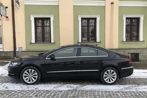 Elegancki, czarny Volkswagen Passat CC na zimowych oponach stoi na ośnieżonej, brukowanej ulicy przed kamienicą z zielonymi oknami.