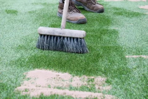 Cepillo extendiendo arena de sílice para césped artificial. Mantenimiento del césped sintético.