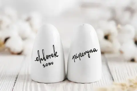 Białe solniczki z napisem "chlorek sodu" i "piperyna" - idealne, by co dać na parapetówkę.