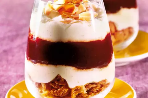 Schichtdessert im Glas mit zerbröselten Amarettini, roter Fruchtsauce und cremiger Masse, garniert mit Mandelblättchen.