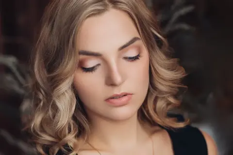 Delikatne, świąteczne makijaże podkreślają urodę blondynki z kręconymi włosami.