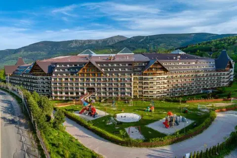 Duży hotel z placem zabaw i widokiem na góry.