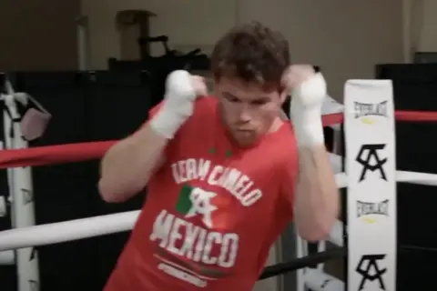 Boxer in a red "Team Canelo Mexico" shirt practices shadow boxing in a ring, his fists wrapped and ready.