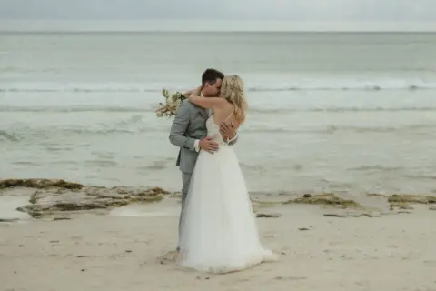 Ein Brautpaar küsst sich am Strand. Sie heiraten auf Mallorca am Strand, umgeben vom Meer und Sand.