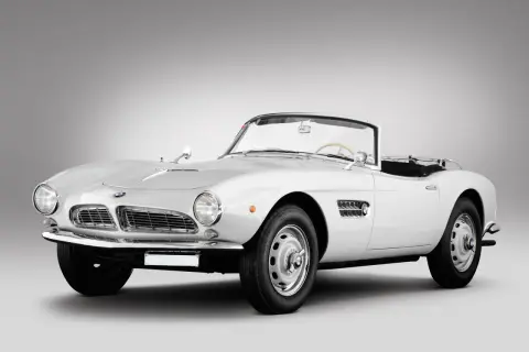Biały kabriolet BMW 507 z lat 50. prezentuje się elegancko na szarym tle.