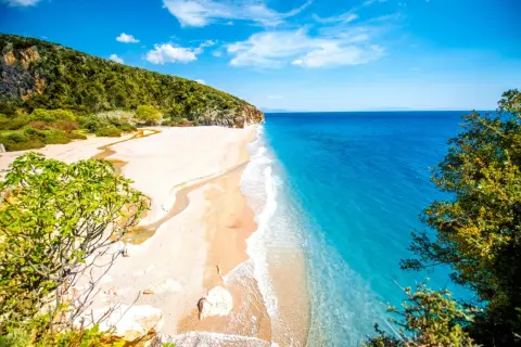 En orörd albanien strand med turkost vatten, vit sand och gröna kullar. En liten flod rinner ut i havet.
