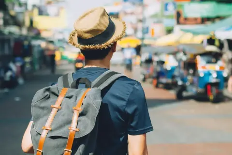 Mężczyzna w kapeluszu i z plecakiem na tle tętniącego życiem azjatyckiego miasta. Poznaj jego travel hacks!