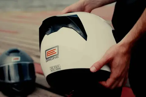 Ręce trzymają biały kask motocyklowy. Obok leży czarny kask. Dylemat: kask szczękowy czy integralny?