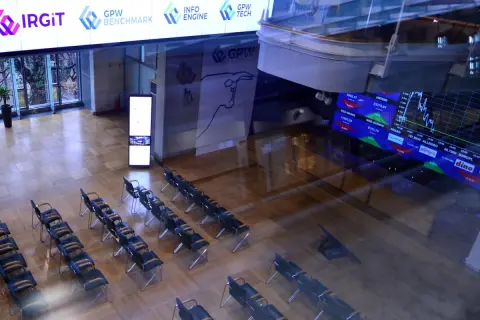 Sala konferencyjna z rzędami krzeseł, na ekranach widoczne dane giełdowe, w tym knf rejestr pozycji krótkich.