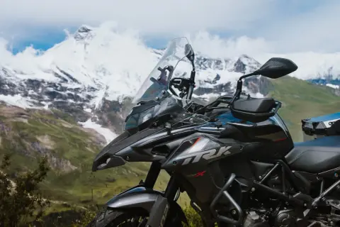 Ciemny motocykl turystyczny na tle ośnieżonych gór i zielonej doliny.