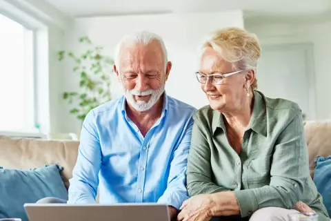 Uśmiechnięta para seniorów sprawdza w internecie, ile wynosi renta inwalidzka w Niemczech.