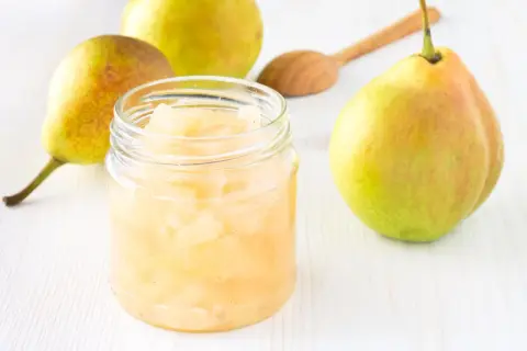 Glas mit Birnenmus, daneben frische Birnen und ein Holzlöffel. Perfekt zum Birnen einkochen.