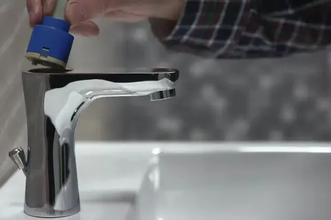 Dłoń wkłada niebieski wkład do chromowanego kranu.