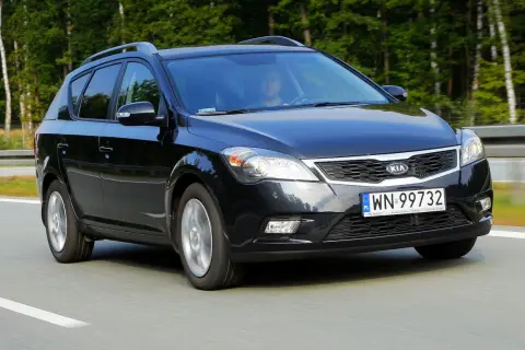Czarny Kia Ceed 1. kombi jedzie po drodze, otoczony zielenią.