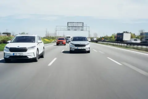 Na autostradzie biały i srebrny SUV jadą z zachowaniem bezpiecznej odległości między samochodami na światłach.