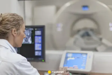 Lekarka w białym fartuchu analizuje obraz z rezonansu magnetycznego na monitorze.