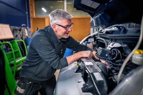Mekaniker med glasögon arbetar med att serva bilens motor.