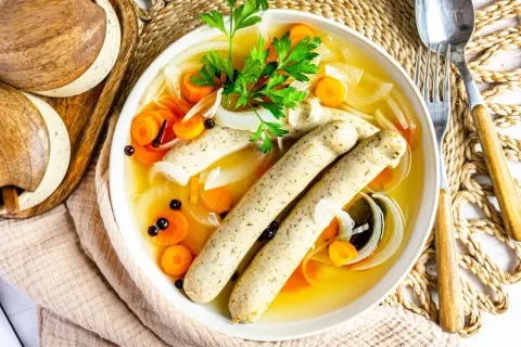 Herzhaftes rezept blaue zipfel: zwei Würste in Brühe mit Karotten, Zwiebeln und Petersilie.