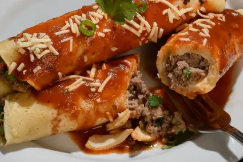 Pyszne naleśniki po meksykańsku z mielonym mięsem, polane sosem pomidorowym i posypane serem.