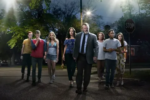 En grupp människor, inklusive rollistan i Mr. Mercedes, går mot kameran på en mörk gata under en gatlykta.