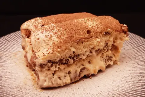 Une part de tiramisu au café, saupoudrée de cacao, sur une assiette striée. Un délice qui invite à découvrir la recette.