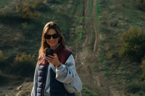 Kobieta z telefonem na tle pagórkowatego krajobrazu, idealnego do **roaming Wielka Brytania**.