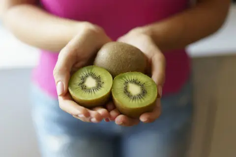 Dłonie trzymają całe i przekrojone kiwi. Ten owoc to naturalny sposób na zaparcia.