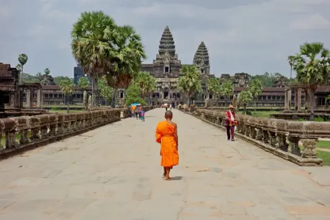 Mnich w pomarańczowej szacie idzie w stronę Angkor Wat, symbolu kambodżańskiej wycieczki.