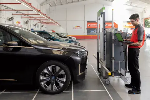 Técnico en taller revisa datos en laptop para calibrar máquina de corte de lunas de autos.