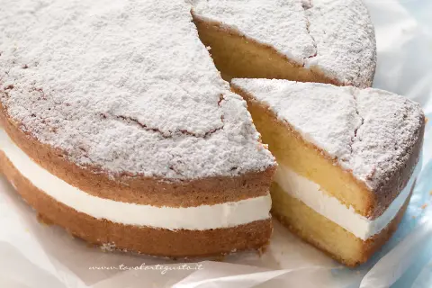 Una soffice torta kinder paradiso, spolverata di zucchero a velo, con una golosa crema bianca tra due strati di pan di Spagna.