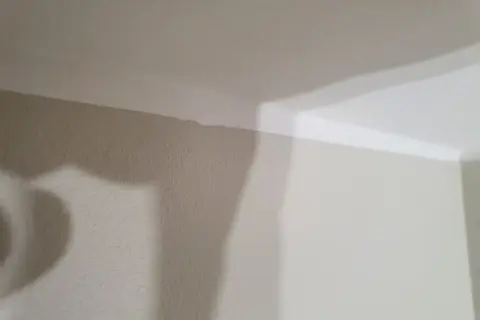En snedtakad vägg med en ojämn kant där taket möter väggen. En skugga faller över väggen.