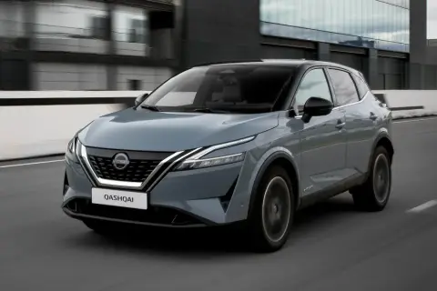 Grå Nissan Qashqai kör på en väg, en del av ett nissan qashqai test. Moderna byggnader syns i bakgrunden.