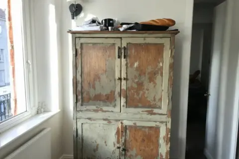 Vieil armoire en bois patiné, prêt à être customisé. Une baguette repose sur le dessus.