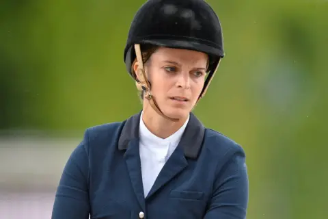 Athina Onassis w kasku i eleganckim stroju jeździeckim, skupiona na zawodach.