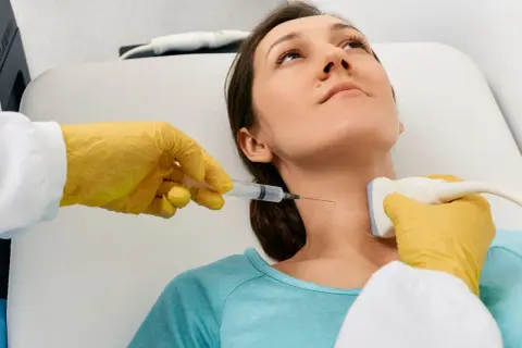 Lekarz wykonuje biopsję cienkoigłową tarczycy, używając aparatu USG do precyzyjnego nakłucia.