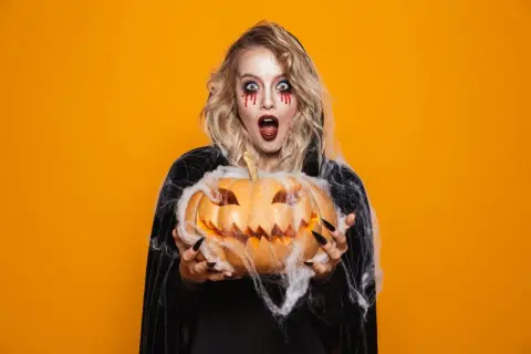 Przerażająca dziewczyna z makijażem na imprezę halloween trzyma wydrążoną dynię.